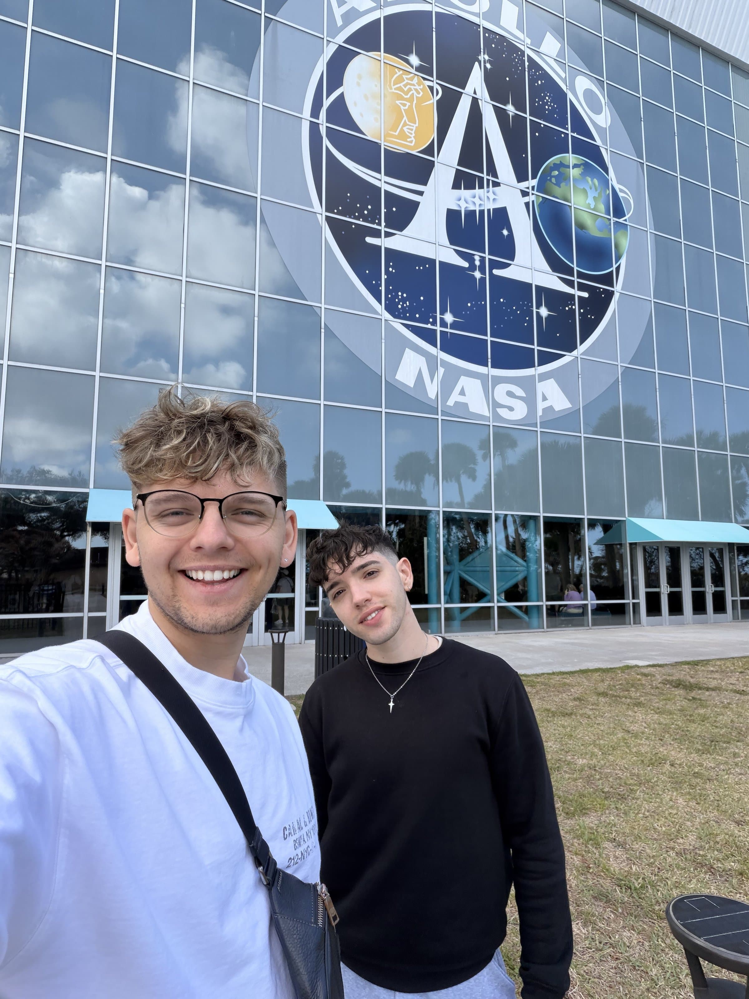 Corey and Damian smiling in front of the Apollo NASA logo